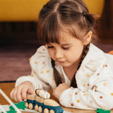 Child playing with the PlanToys blue wooden hybrid train on a rubber road. Three carriage train with magnetic connections. 
