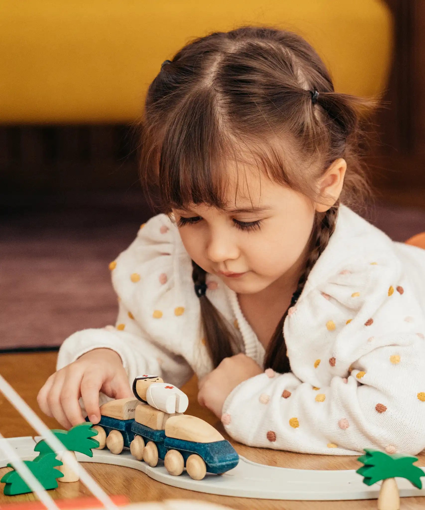 Child playing with the PlanToys blue wooden hybrid train on a rubber road. Three carriage train with magnetic connections. 