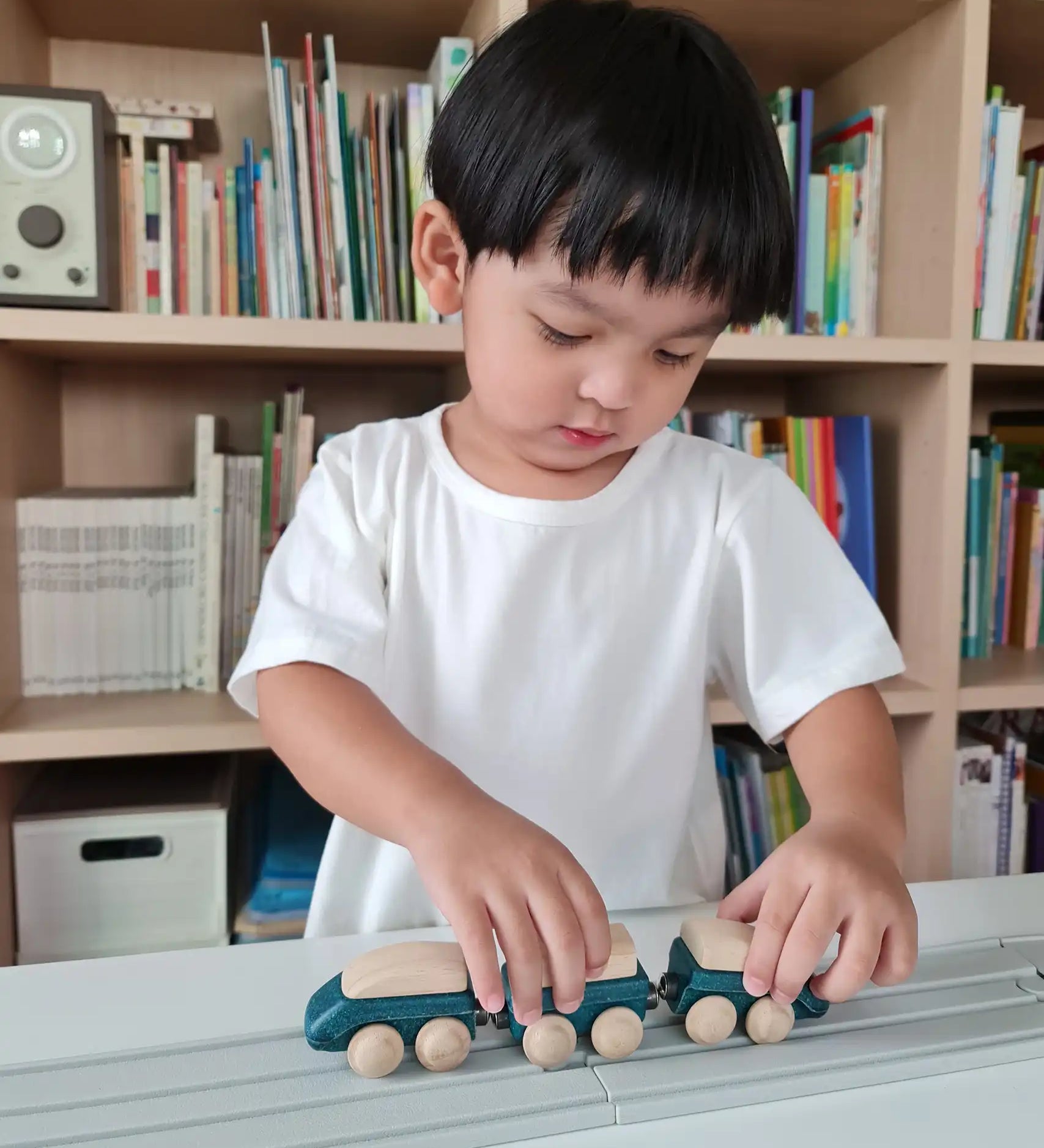 Child playing with the PlanToys blue wooden hybrid train on the PlanToys rubber railway and road. Three carriage train with magnetic connections. 