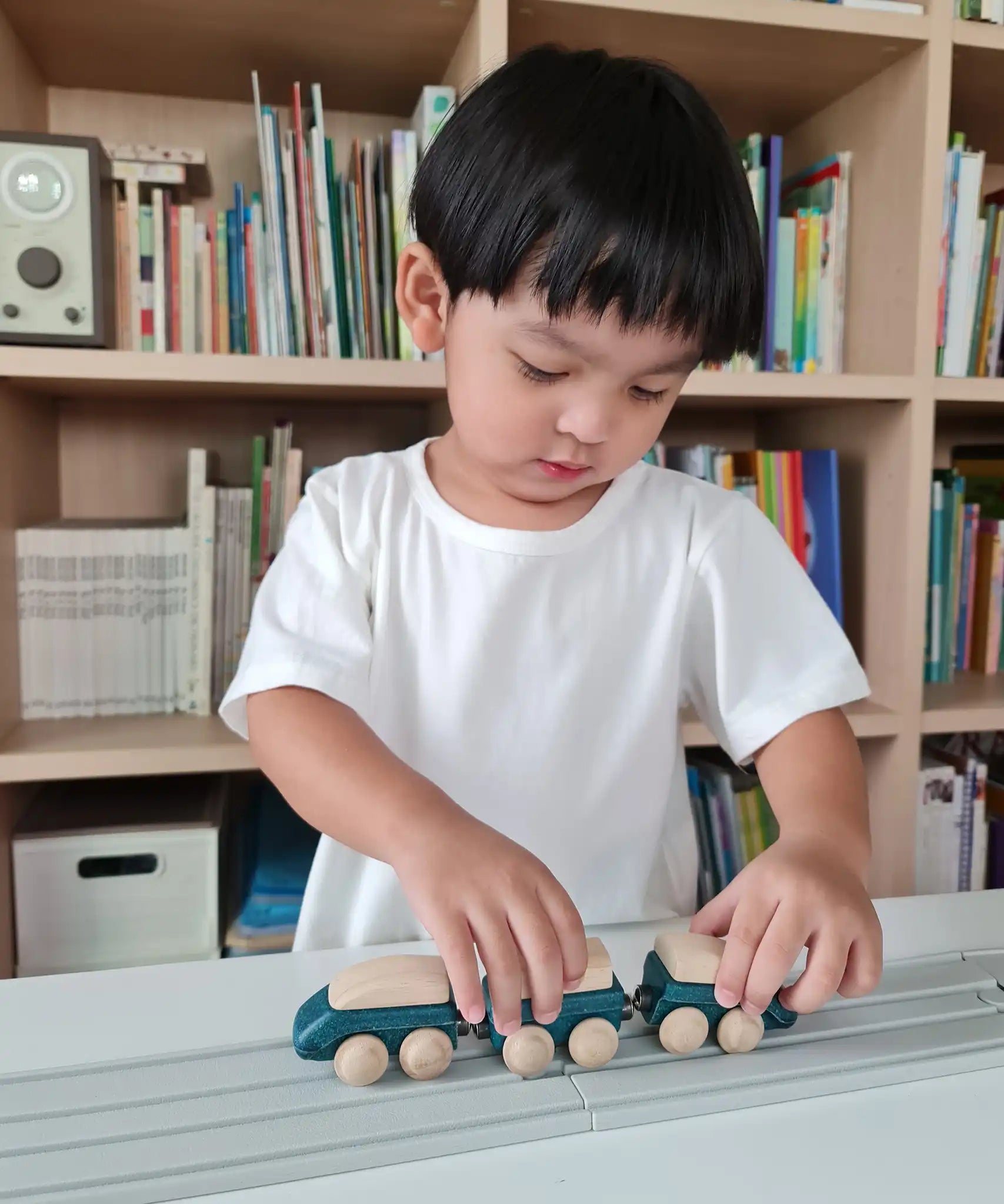 Child playing with the PlanToys blue wooden hybrid train on the PlanToys rubber railway and road. Three carriage train with magnetic connections. 