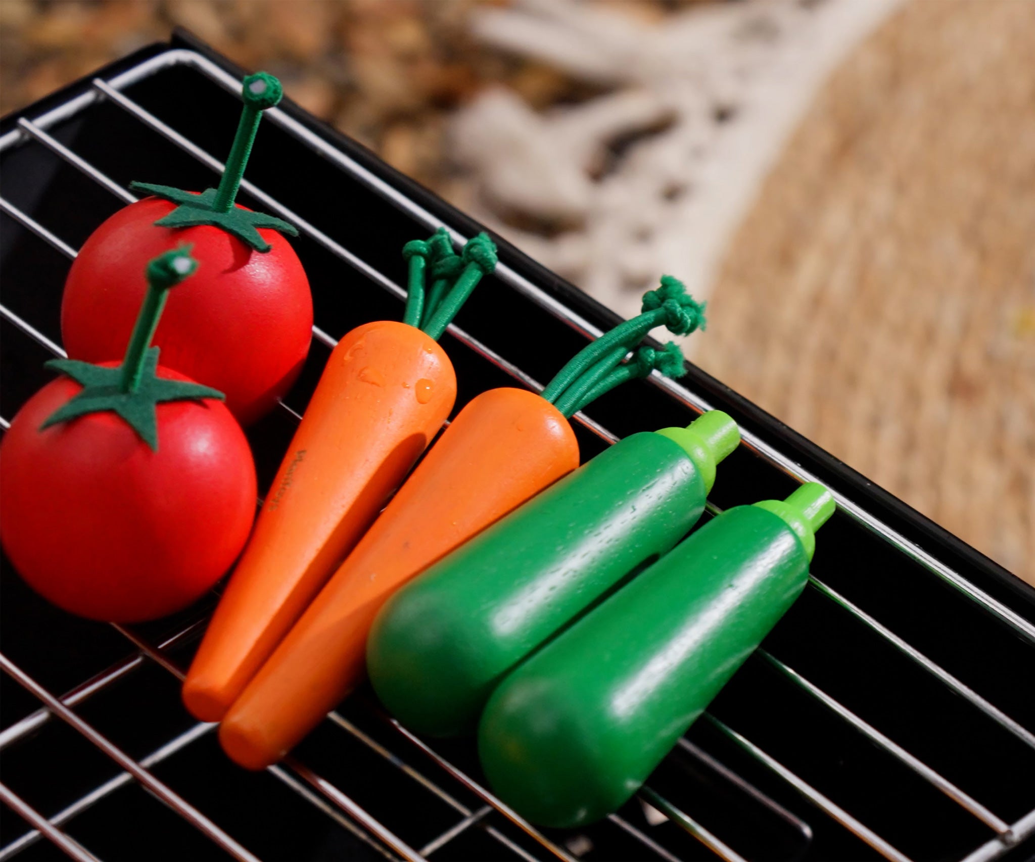 Plan Toys Vegetable Produce Set - Carrots, Courgettes & Tomatoes. The wooden play food is shown on a grill. 