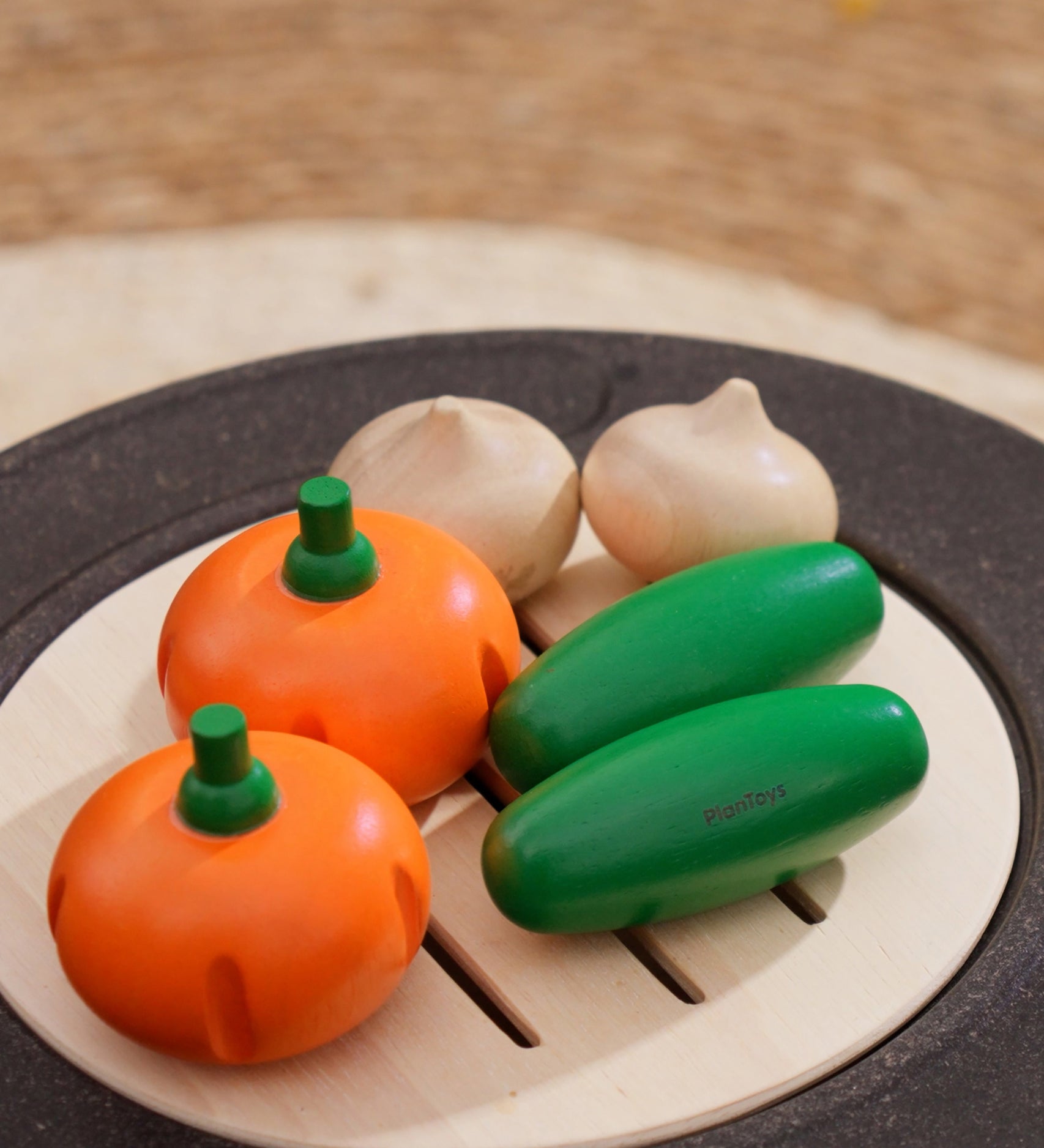 The PlanToys Vegetable Produce Set with Cucumbers, Onions & Pumpkin play food placed on a wooden toy grill. 
