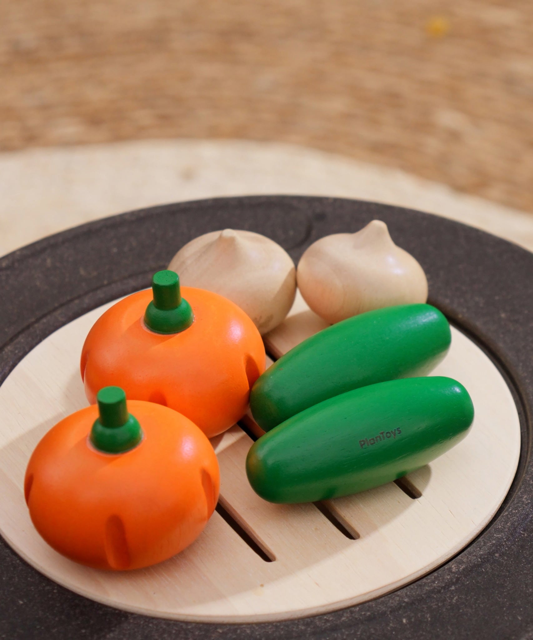 The PlanToys Vegetable Produce Set with Cucumbers, Onions & Pumpkin play food placed on a wooden toy grill. 