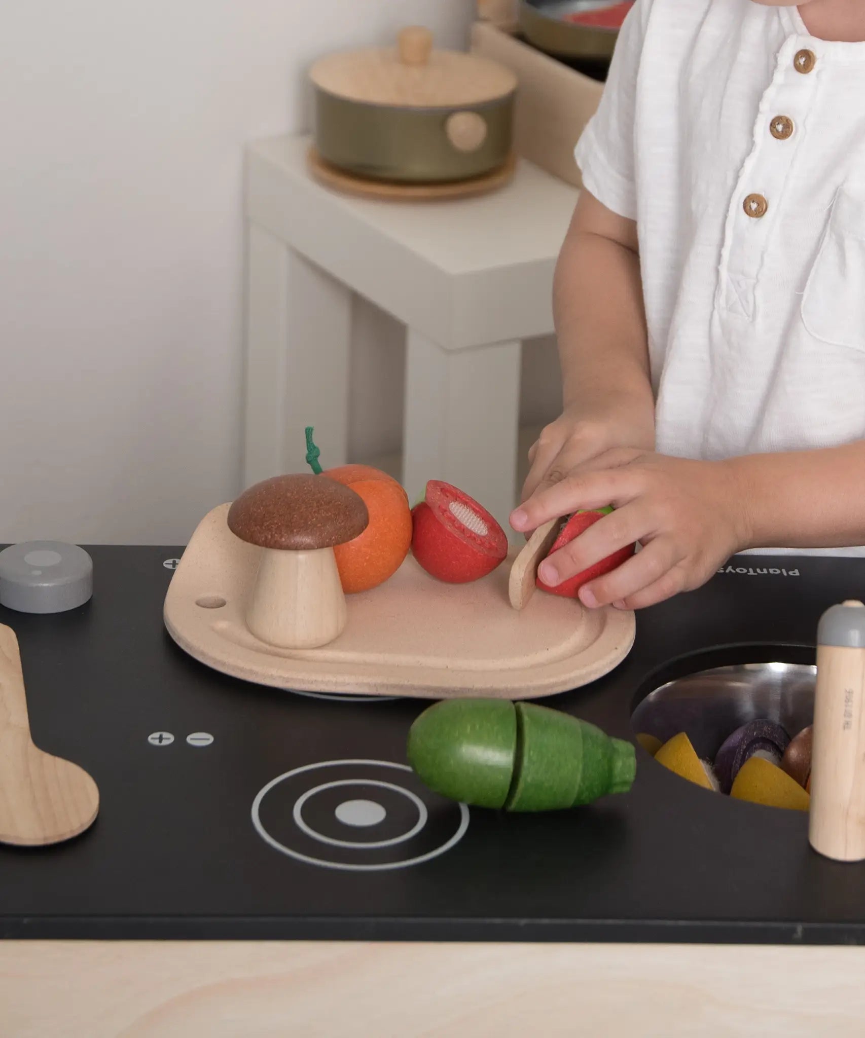 Child playing with the PlanToys wooden veggie set showing a tomato play food cut in half