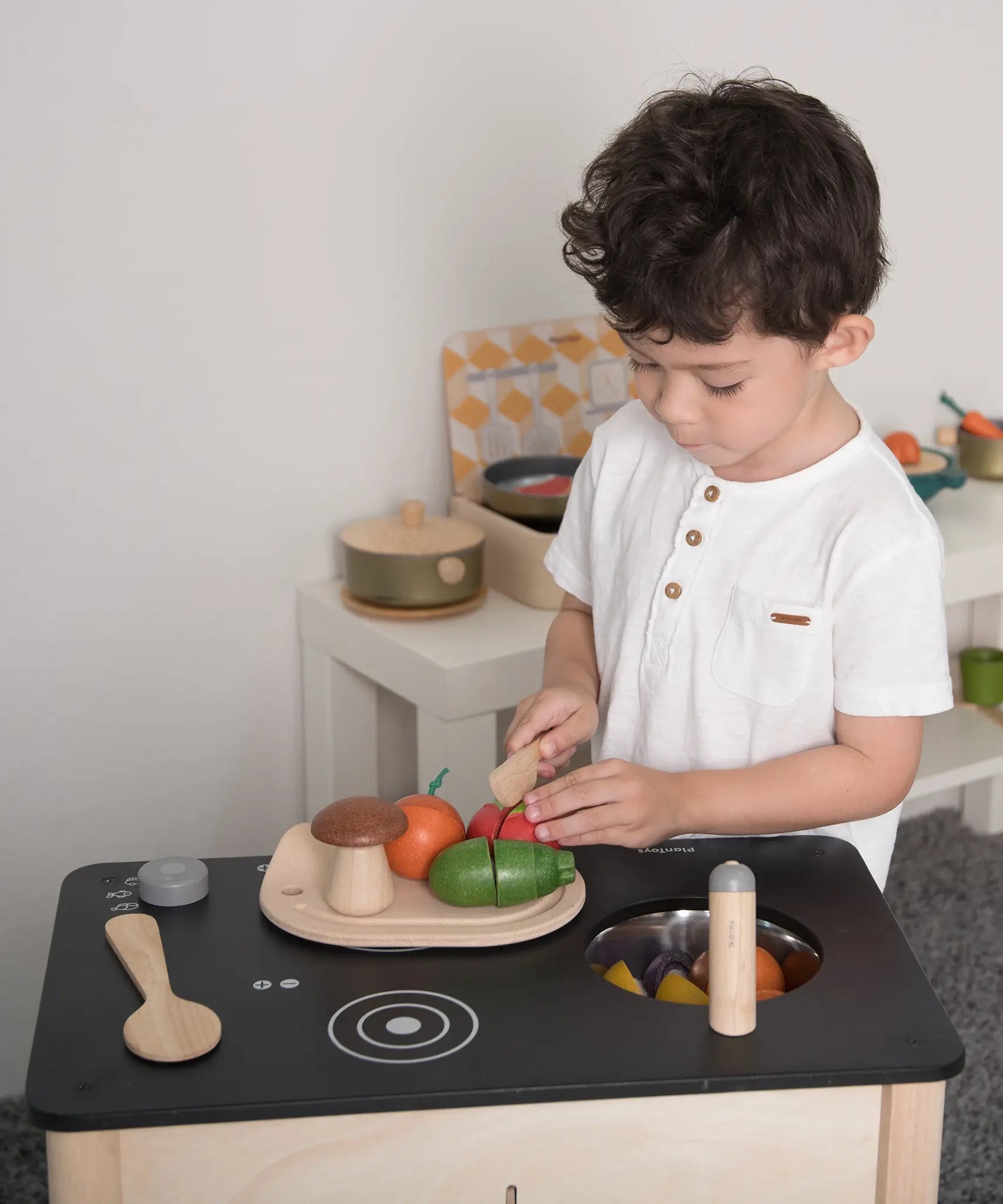 Child prepping veg from the PlanToys wooden veggie set on a play kitchen