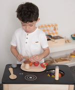 Child playing with the PlanToys wooden veggie set on a play kitchen