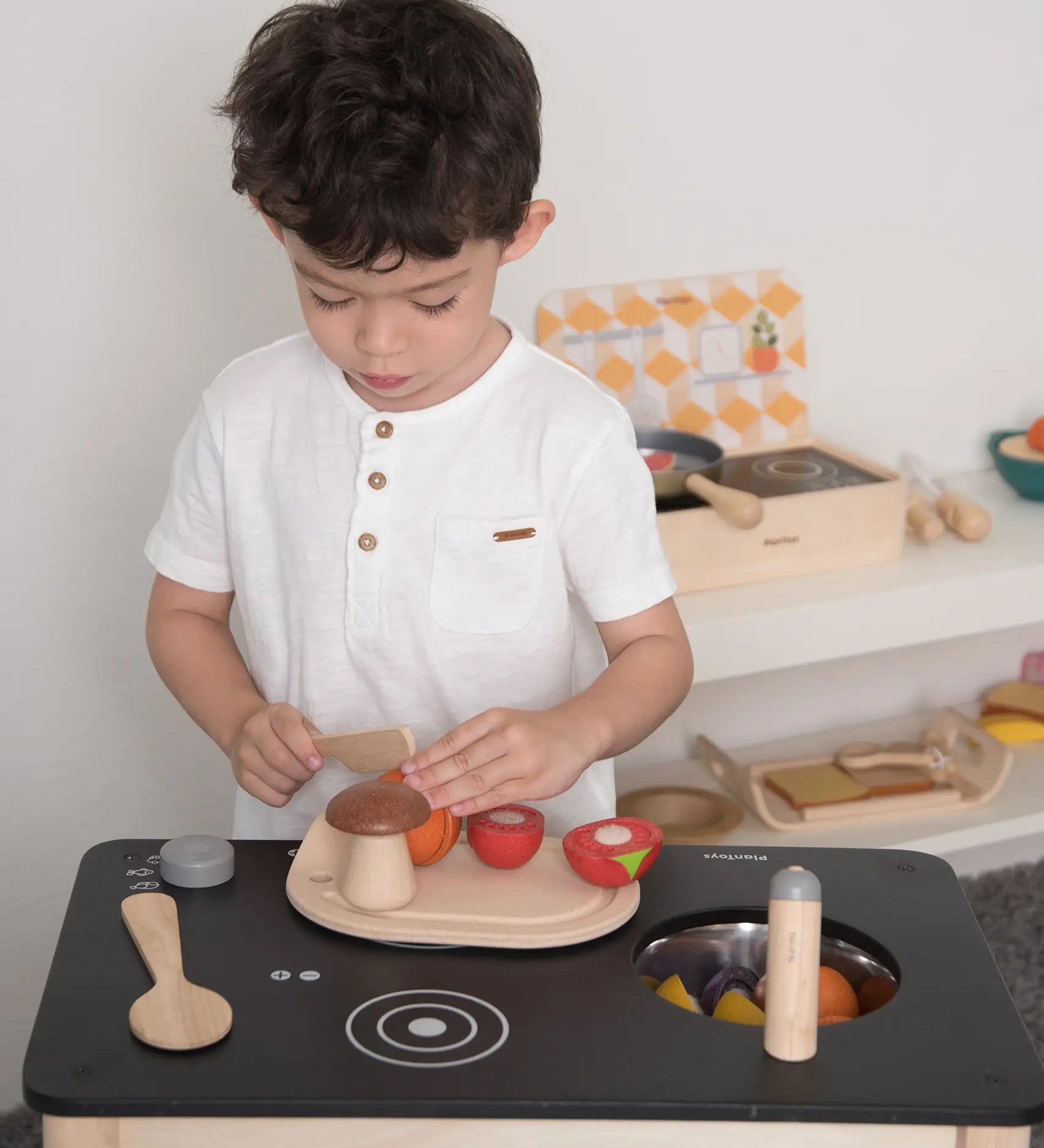 Child playing with the PlanToys wooden veggie set on a play kitchen