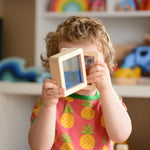 A child holding up two of the squared shaped Plan Toys Water Blocks peeping through them. 