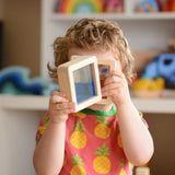 A child holding up two of the squared shaped Plan Toys Water Blocks peeping through them. 