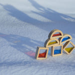 Plan Toys Water Blocks placed outdoors on snow. The reflection of colours from the blocks can be seen on the snow. 
