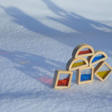 Plan Toys Water Blocks placed outdoors on snow. The reflection of colours from the blocks can be seen on the snow. 
