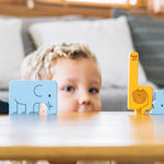 The animal pieces from the PlanToys Animal Puzzle Game
lined up on a wooden surface, a child can be seen Peering through a cap in the middle. 