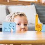 The animal pieces from the PlanToys Animal Puzzle Game
lined up on a wooden surface, a child can be seen Peering through a cap in the middle. 