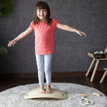 A child standing on an upturned PlanToys Balance Board. The board upturned creates a sort of mini bridge for the child to stand upon. 