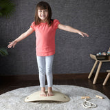 A child standing on an upturned PlanToys Balance Board. The board upturned creates a sort of mini bridge for the child to stand upon. 