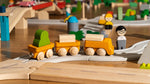 PlanToys yellow wooden cargo train placed on a rubber railway track connected to a wooden road set. 