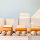 PlanToys yellow wooden cargo train placed on natural wooden blocks. 