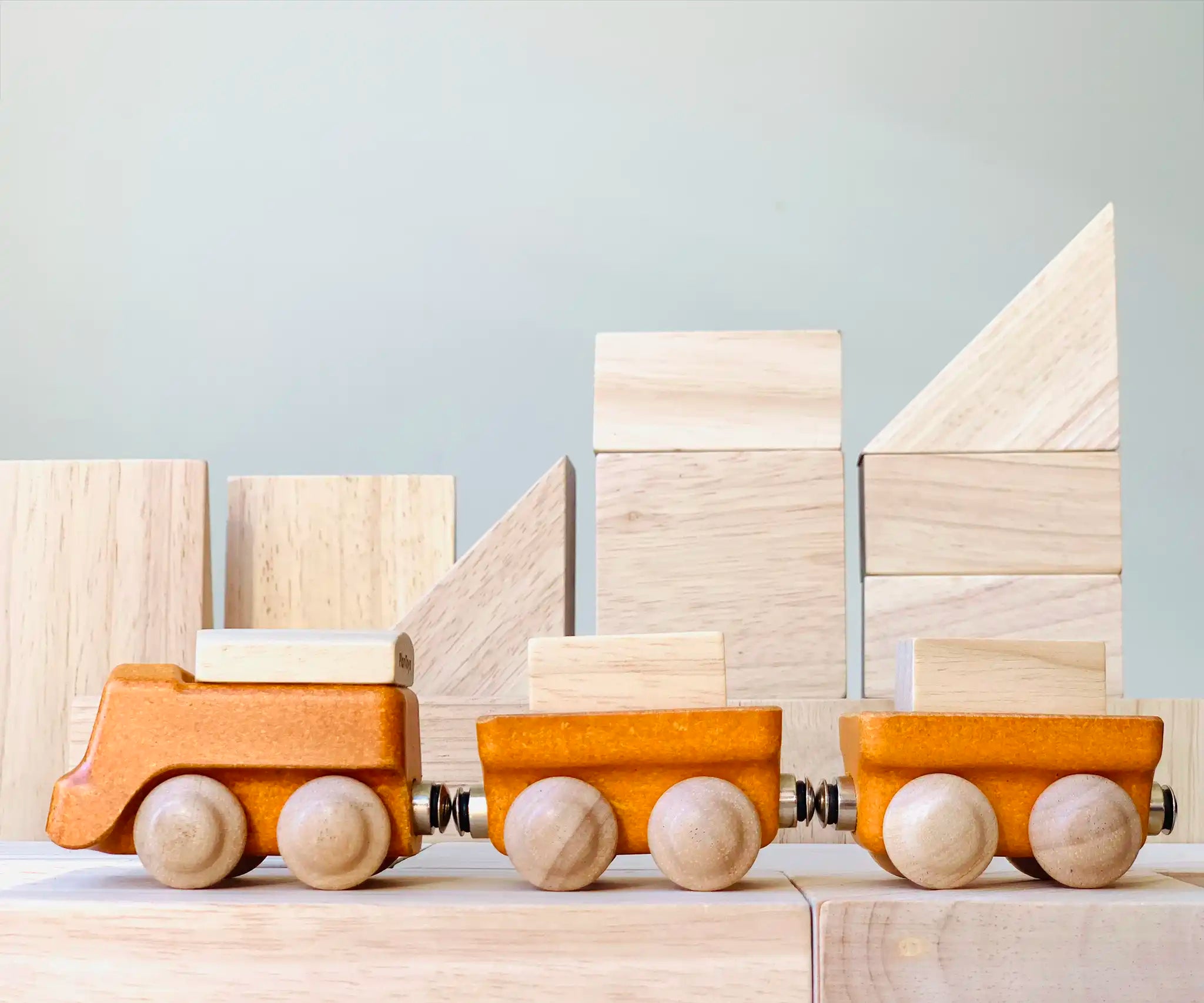 PlanToys yellow wooden cargo train placed on natural wooden blocks. 