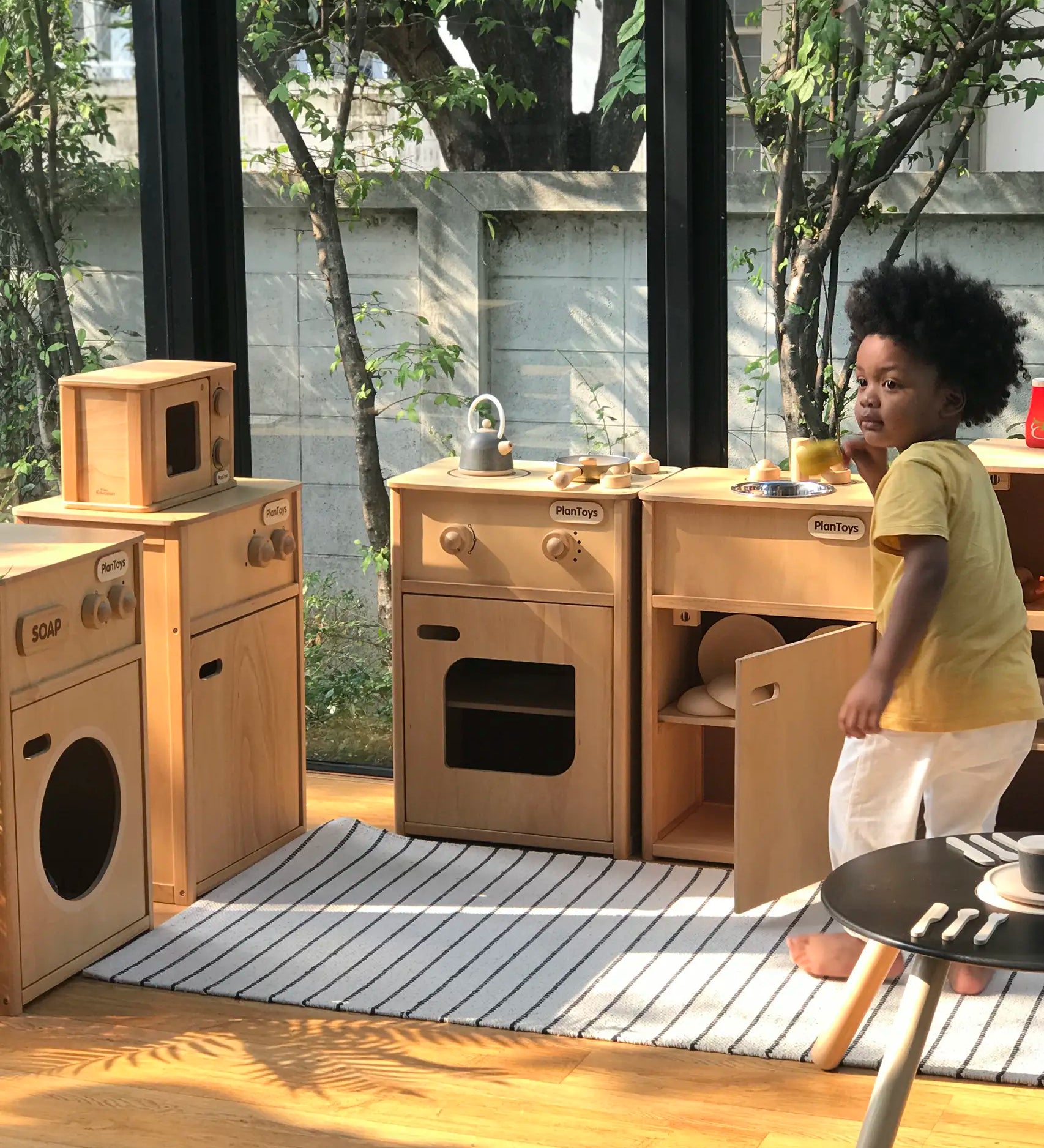 Child playing with different PlanToys wooden play kitchen units