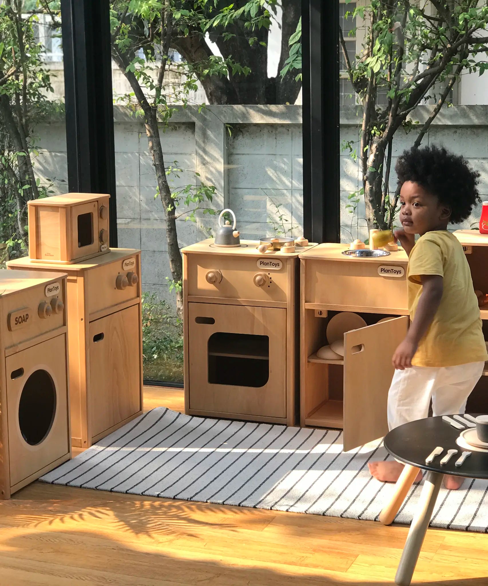 Child playing with different PlanToys wooden play kitchen units
