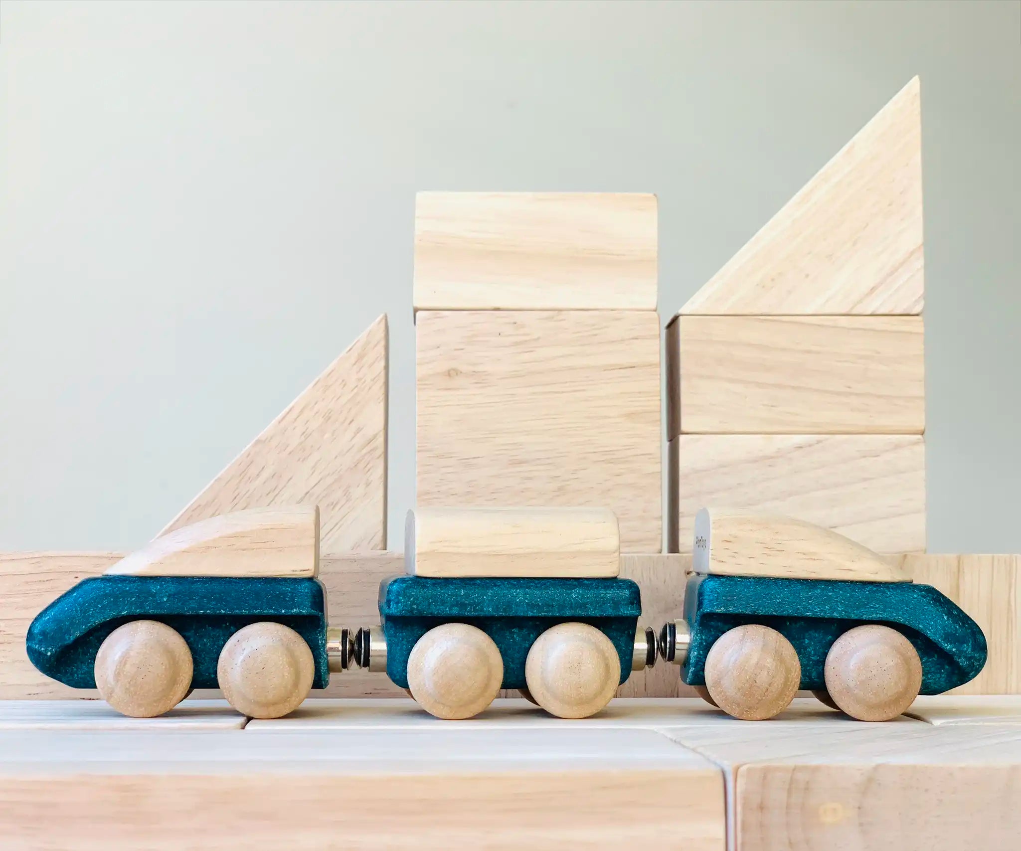 PlanToys blue wooden hybrid train placed on natural wooden blocks. Three carriage train with magnetic connections. 