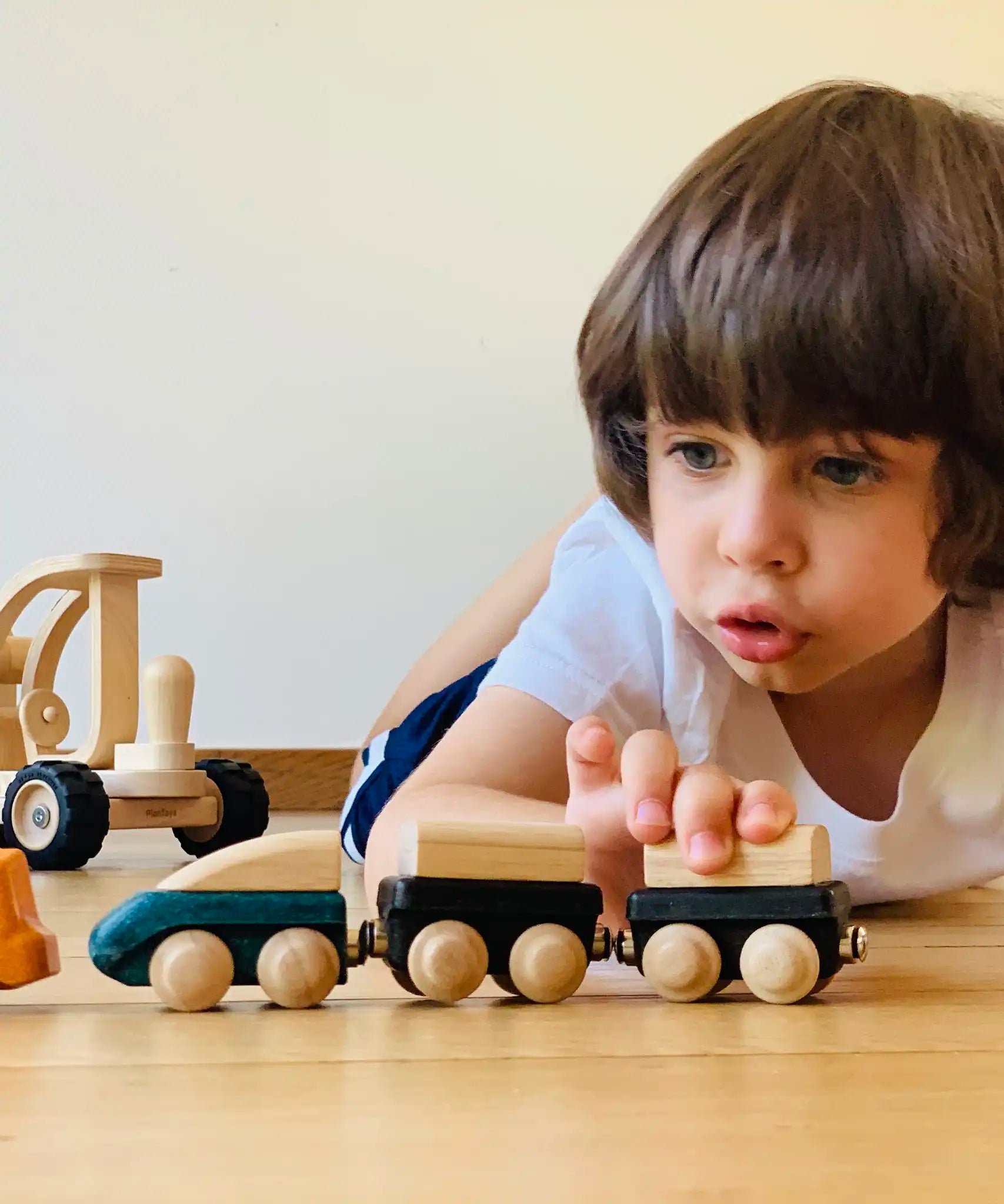 Child playing with the PlanToys wooden trains connecting different colours to each  other. 