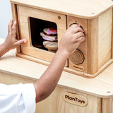 Child playing with the PlanToys wooden microwave play unit with play food inside