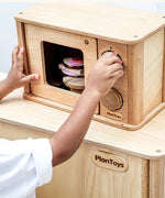 Child playing with the PlanToys wooden microwave play unit with play food inside