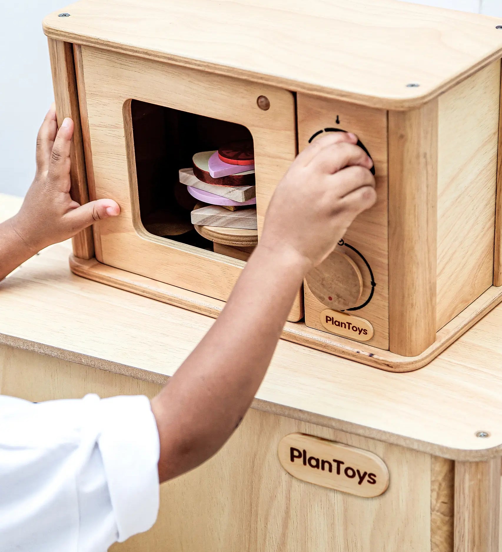 Child playing with the PlanToys wooden microwave play unit with play food inside