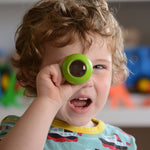 A child holding a green PlanToys Mushroom Kaleidoscope up to their eye. 