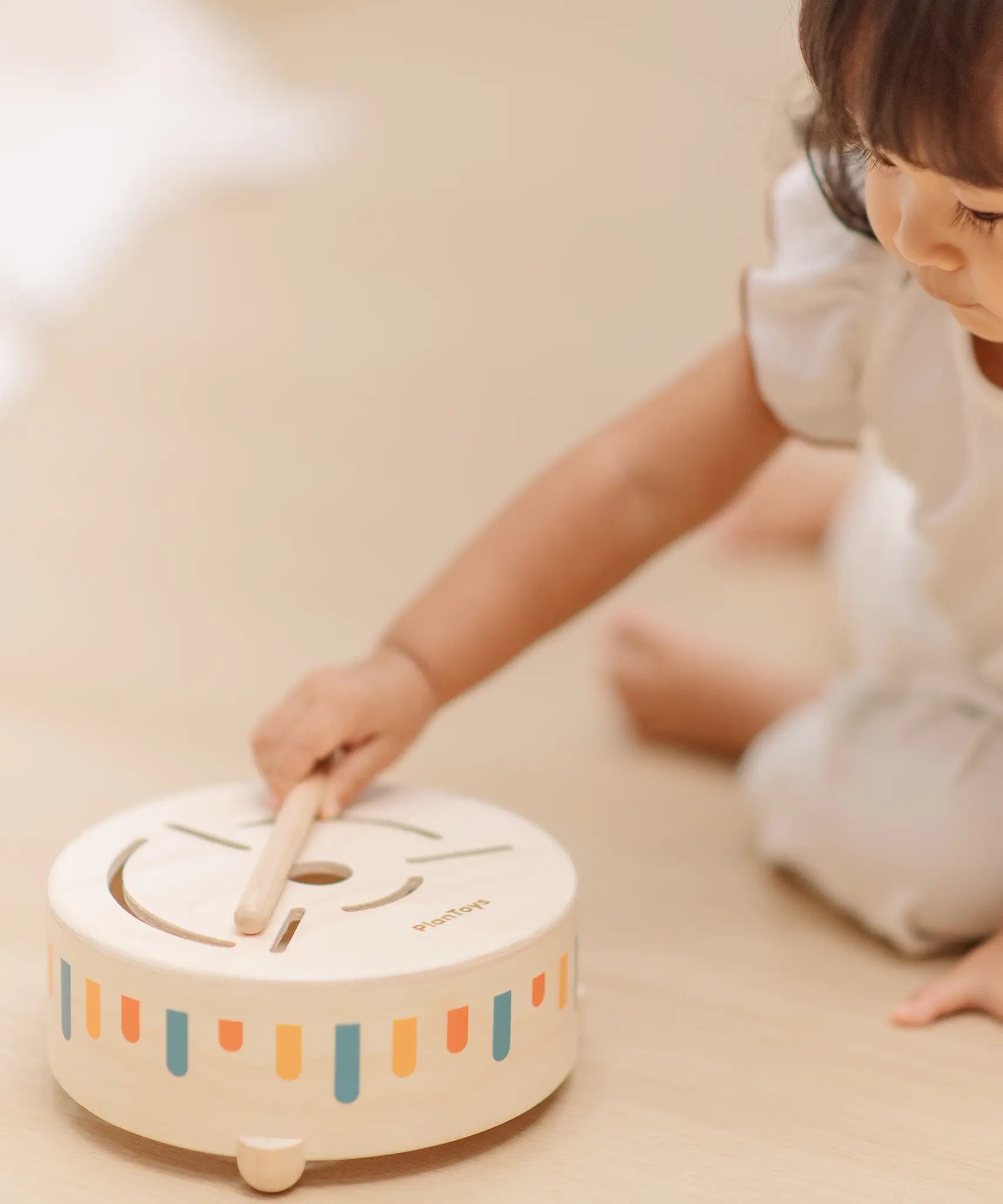 Close up of a child hand placing the wooden drumstick on top of the PlanToys wooden sensory drum musical toy.