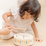 Child playing with the PlanToys wooden sensory drum musical toy, striking the drum with the wood drumstick.