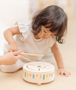 Child playing with the PlanToys wooden sensory drum musical toy, striking the drum with the wood drumstick.