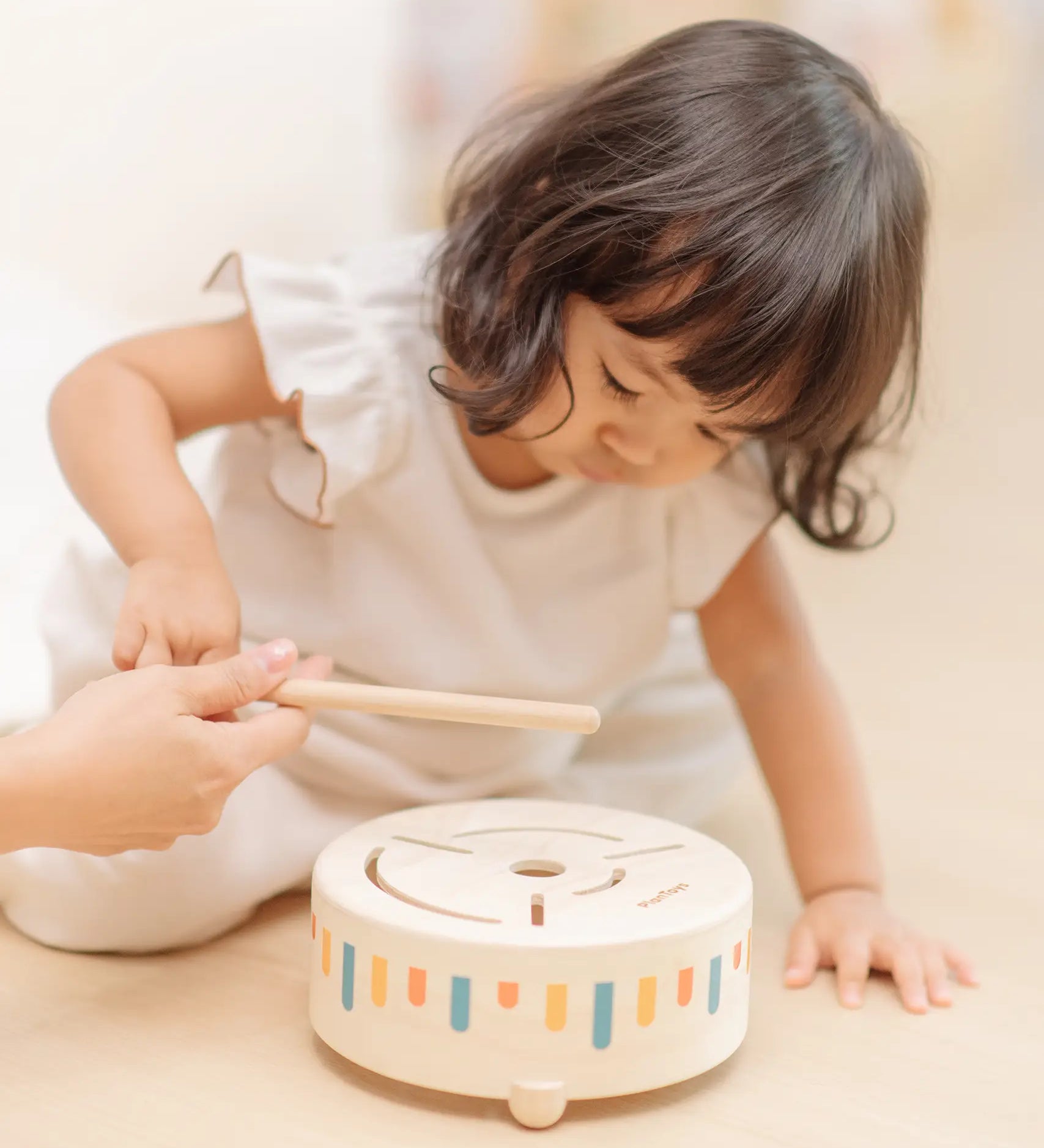 Child playing with the PlanToys wooden sensory drum musical toy, striking the drum with the wood drumstick.