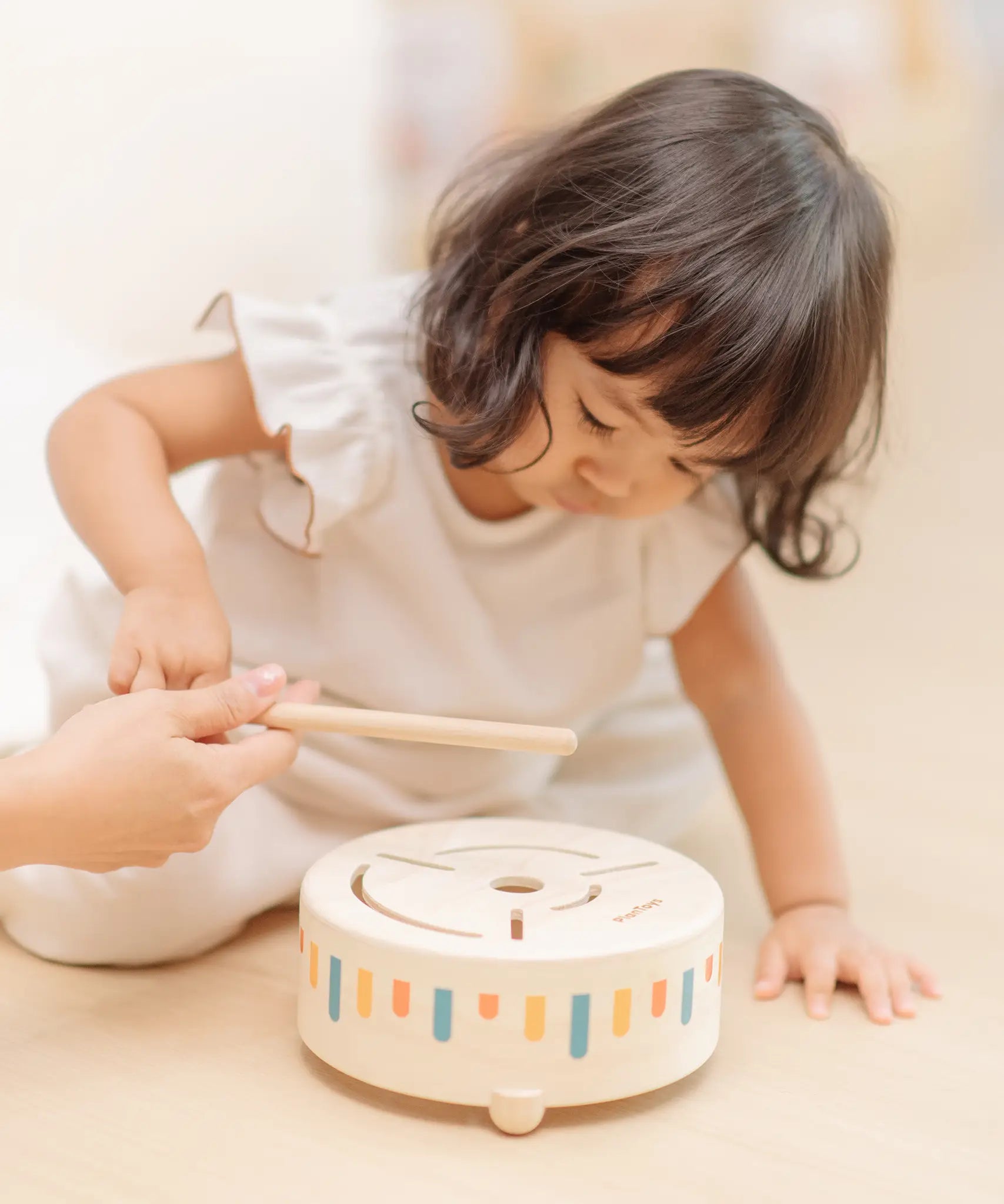 Child playing with the PlanToys wooden sensory drum musical toy, striking the drum with the wood drumstick.