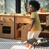 Child playing with different PlanToys wooden kitchen units in the garden