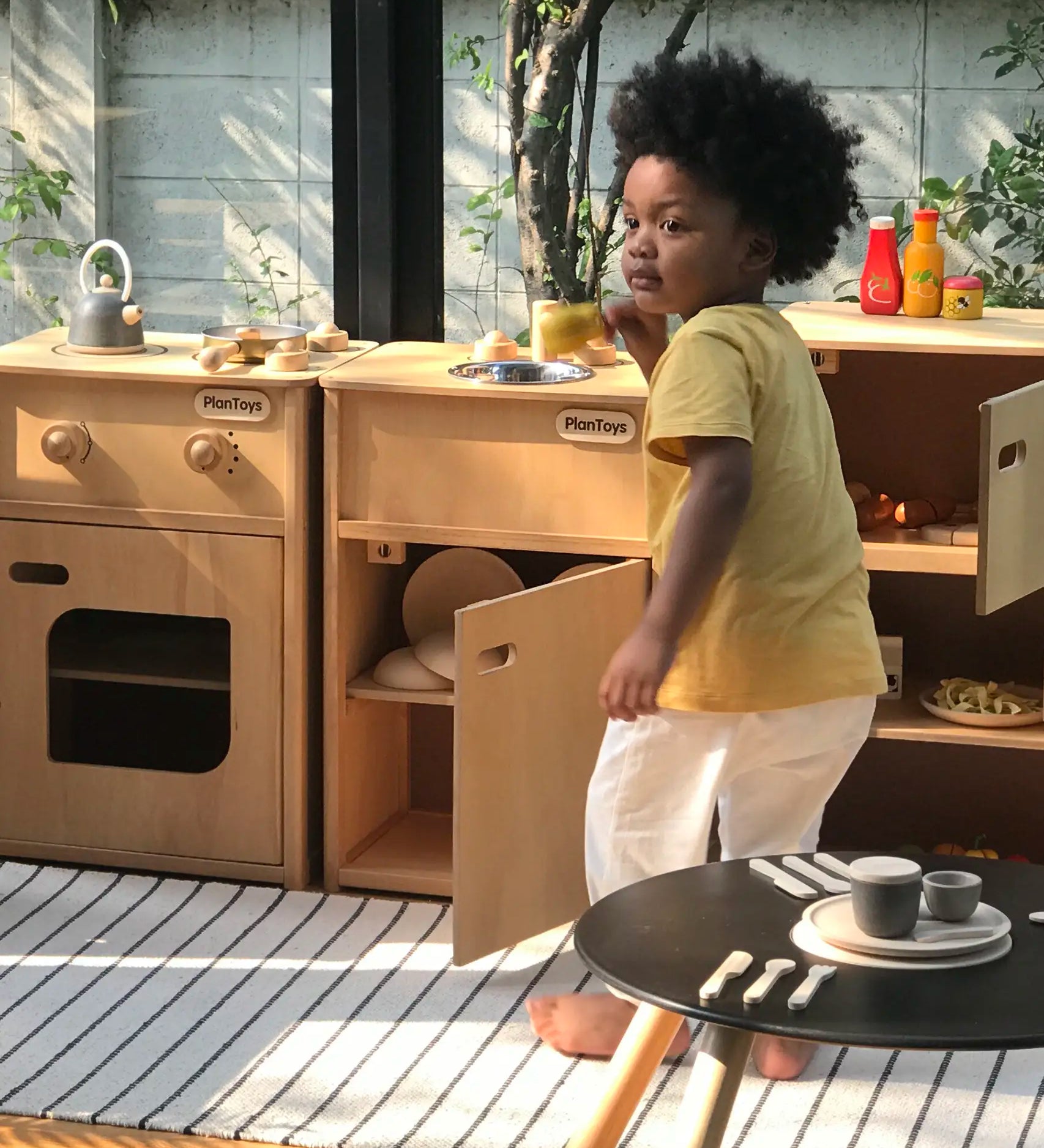 Child playing with different PlanToys wooden kitchen units in the garden
