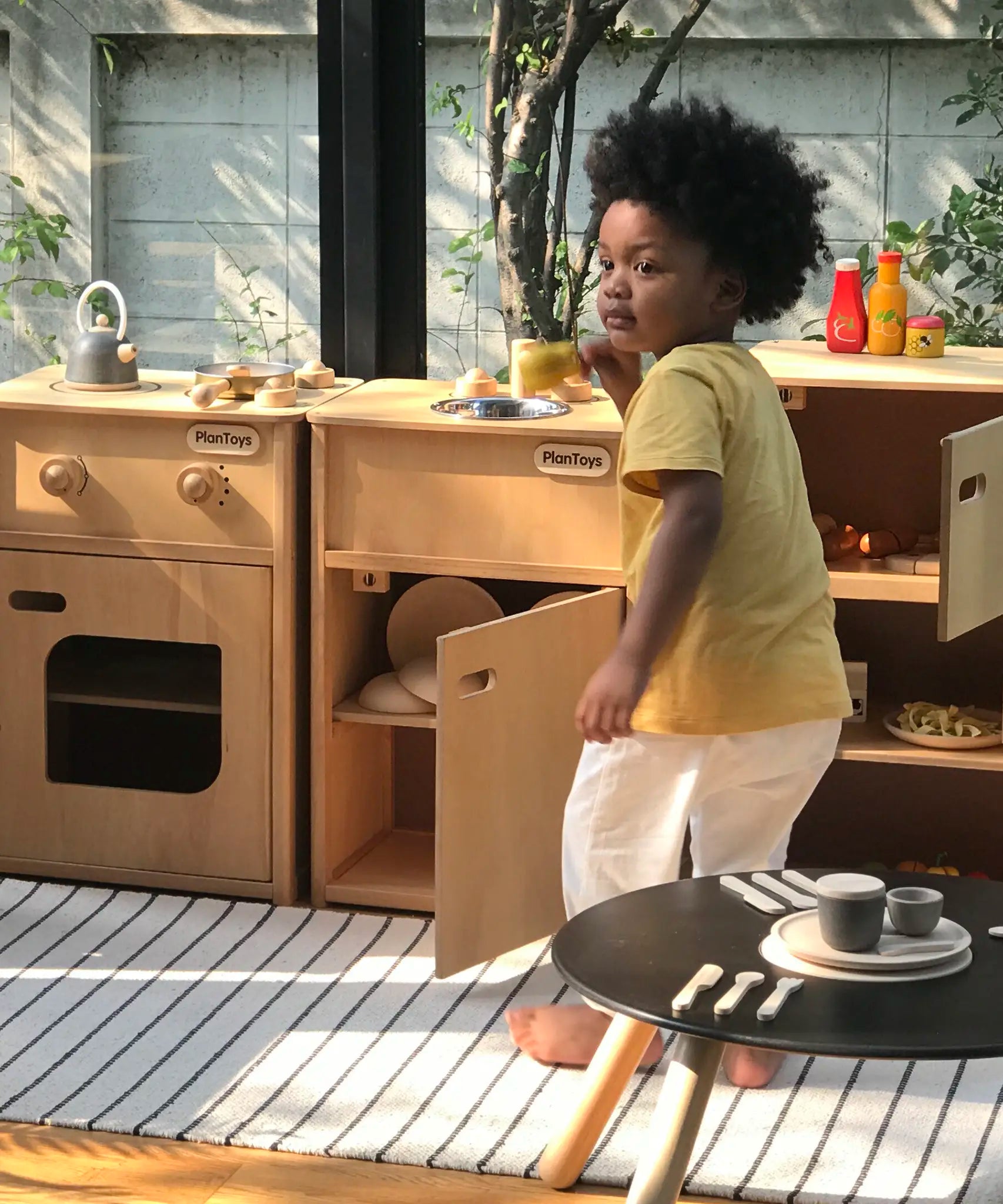 Child playing with different PlanToys wooden kitchen units in the garden