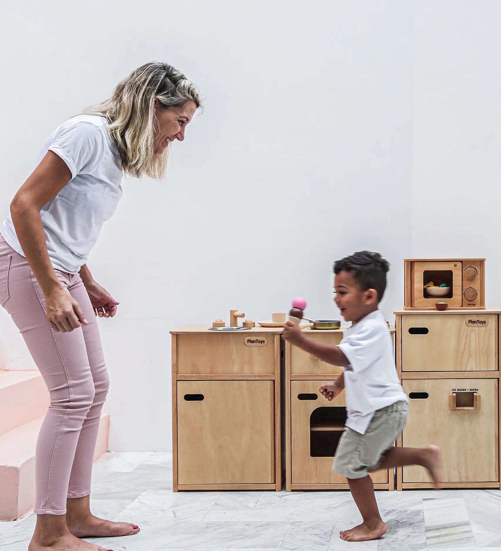Mother and child playing next to different PlanToys wooden kitchen units