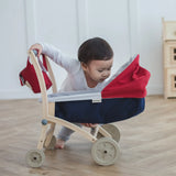 Child looking into a PlanToys stroller with a doll house in the background