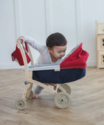 Child looking into a PlanToys stroller with a doll house in the background