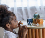 The PlanToys Bee Hives in the Orchard colour way placed side table. A child can be seen crouching in front of the table taking a close look at the bees.