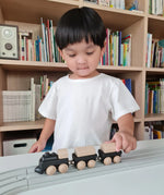 Child pushing the PlanToys black wooden classic toy train along a rubber railway track. 