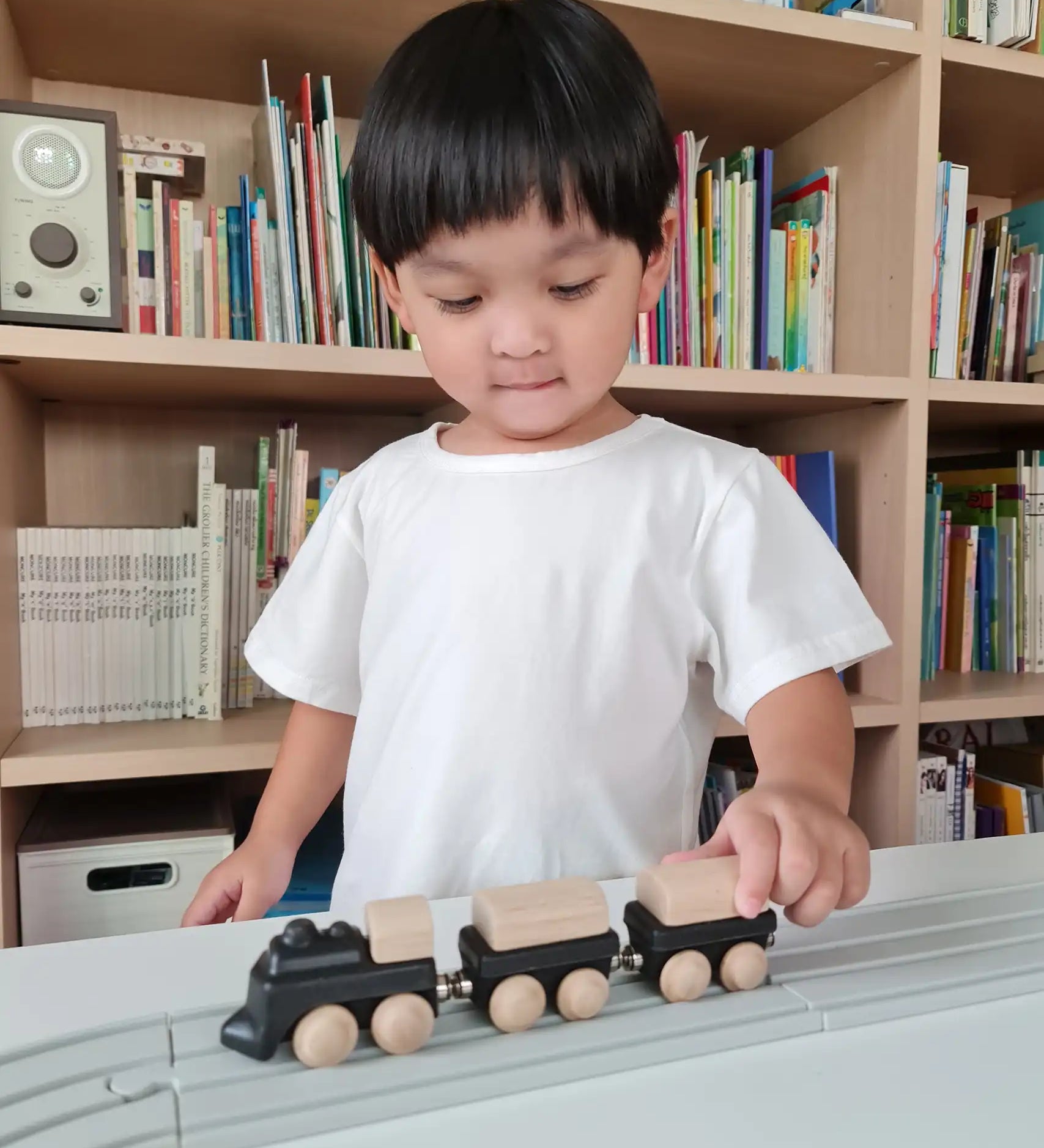 Child pushing the PlanToys black wooden classic toy train along a rubber railway track. 