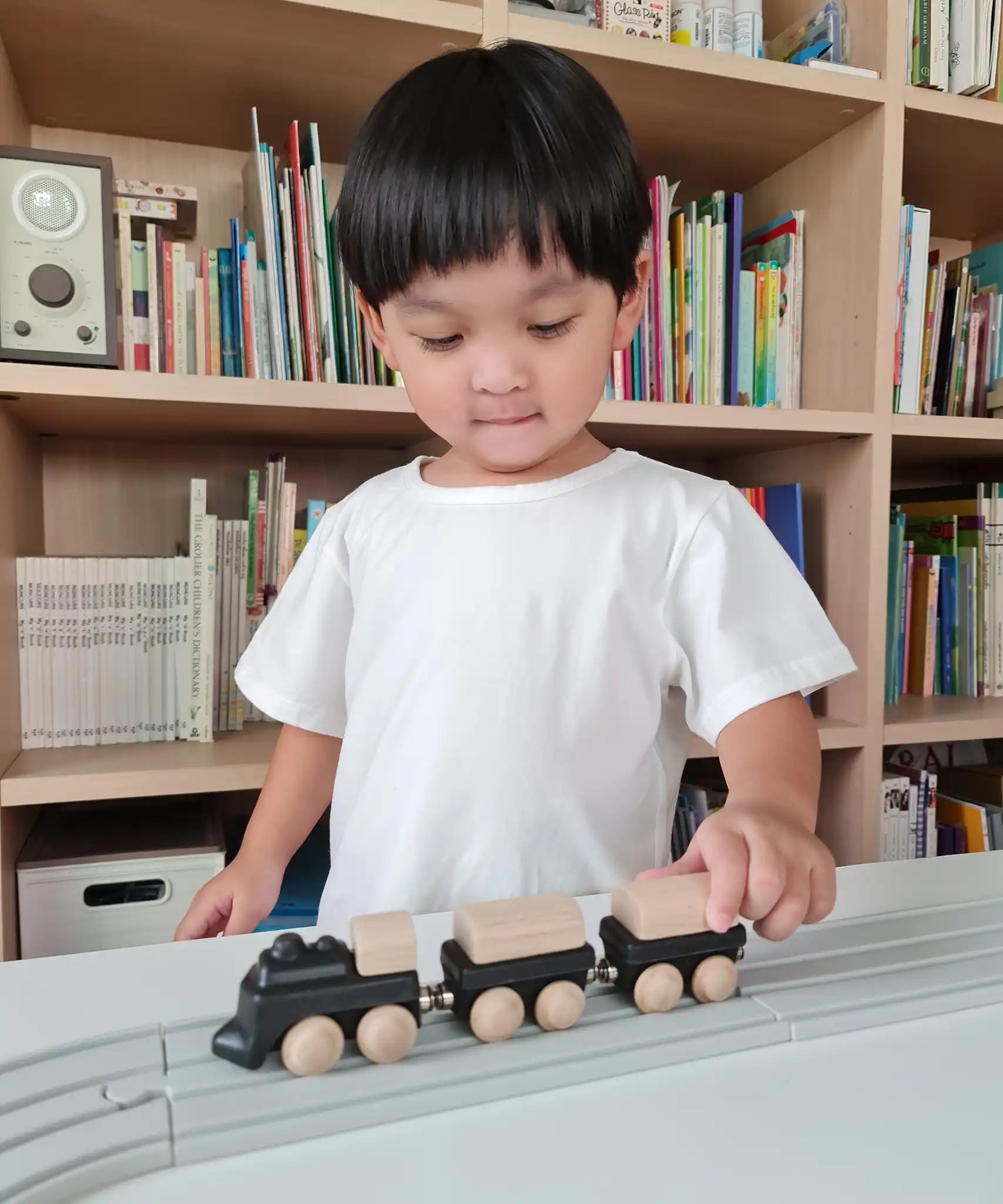 Child pushing the PlanToys black wooden classic toy train along a rubber railway track. 