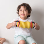 Child playing the Plan Toys Musical Concertina toy sat on a rhythm box.