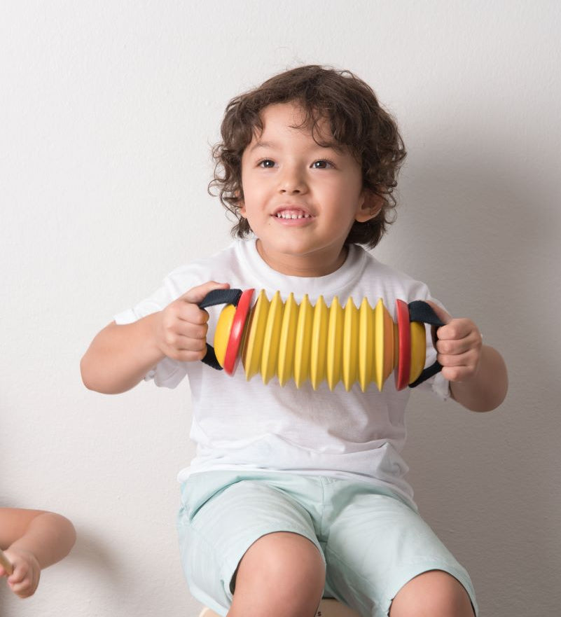 Child playing the Plan Toys Musical Concertina toy sat on a rhythm box.
