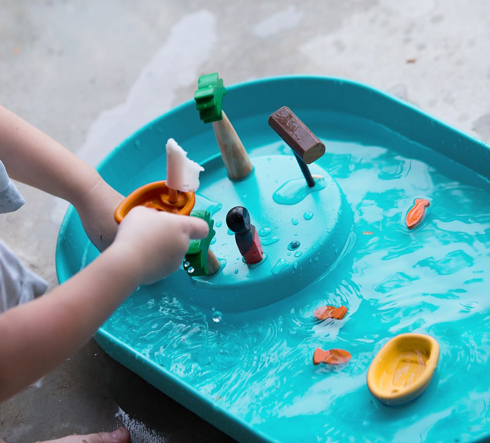 A close up of a child's hand playing with the PlanToys Water Play Set. 