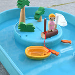 A close up of the raised section of the PlanToys Water Play Set. The wooden tree and doll figures have been placed on the raised section. The yellow boat has been anchored to the wooden post. Two orange fish can be seen in the water.
