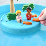 A close up of the raised 'island' section of the PlanToys Water Play Set. The two dollies are on the island surrounded by the trees and greenery and three orange fish. 